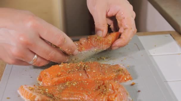 Een stuk verse rode vis wordt bestrooid met specerijen en zout in slow motion van dichtbij bekeken. Zalmsteak op smaak brengen. Chef wrijft de biefstuk met zijn handen voor het bakken. - Video