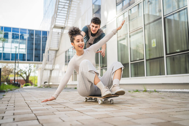 Junge Mann und Frau Teenager-Paar kaukasischen Bruder und Schwester haben Spaß auf Skateboard schieben, um durch das moderne Gebäude in Tag glücklich lächeln echte Menschen Familie Liebe Konzept kopieren Raum - Foto, Bild