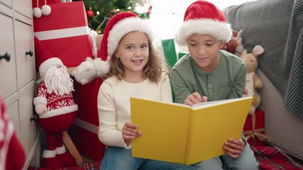 Αξιολάτρευτο αγόρι και κορίτσι ανάγνωση βιβλίο γιορτάζει τα Χριστούγεννα στο σπίτι - Πλάνα, βίντεο