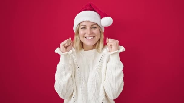 jonge blonde vrouw het dragen van kerst hoed klappen handen applaus over geïsoleerde rode achtergrond - Video