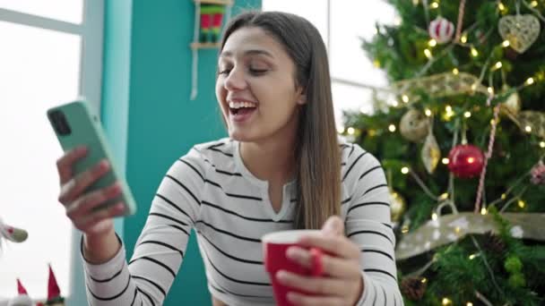 Jonge mooie Spaanse vrouw met behulp van smartphone het drinken van koffie vieren kerst thuis - Video
