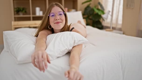 Молодая блондинка, уверенно улыбающаяся, лежа на кровати, выглядит сексуально в спальне - Кадры, видео