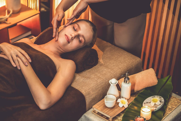 Kaukaska kobieta ciesząca się relaksujący masaż głowy anty-stres i rozpieszczające piękno twarzy rekreacji rekreacyjnej skóry w ciepłym świetle świec ambient salon spa w luksusowym ośrodku lub hotelu. Cichy zapach - Zdjęcie, obraz