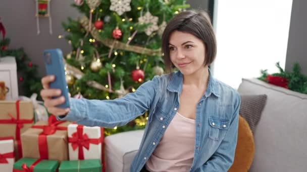 Mladý kavkazský žena přičemž selfie s smartphone stojící u vánočního stromku doma - Záběry, video