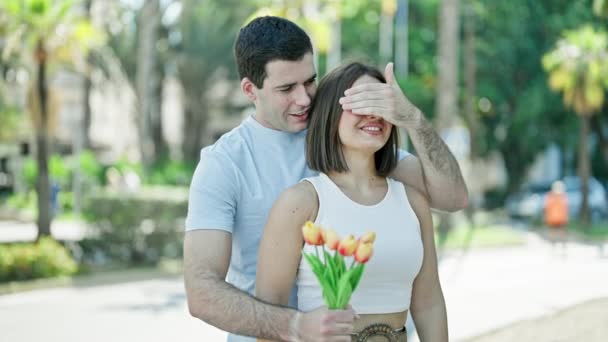 Mooi paar verrassing met boeket van bloemen bedekking ogen knuffelen elkaar in het park - Video