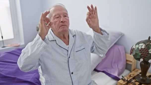 Vrolijke oudere man, rustig zittend in de slaapkamer, verzonken in mindful yoga meditatie. sportpyjama 's, ogen zacht gesloten, gebaren fluisteren rust. een portret van kalme rijpheid. - Video