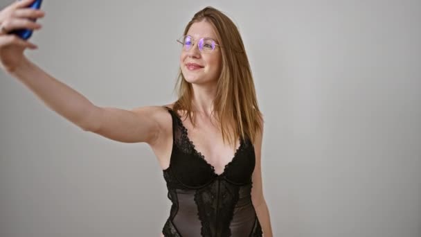 Mladá blondýna žena hledá sexy, aby selfie smartphone s úsměvem přes izolované bílé pozadí - Záběry, video