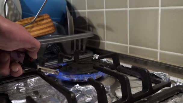 Hand zündet einen Gasherd mit einem Feuerzeug an und stellt einen alten türkischen Kaffeewärmer darauf. Mittlerer Schuss in der Küche, das Metallgeschirr auf die schmutzige Herdplatte zu stellen, abgedeckt mit Silberfolienpapier. - Filmmaterial, Video