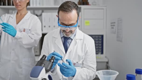 Deux scientifiques souriants, compagnons de science, versant du liquide dans une éprouvette à l'aide d'une pipette dans un laboratoire intérieur, zooment sur leurs gants de sécurité pendant qu'ils découvrent ensemble une nouvelle analyse médicale. - Séquence, vidéo