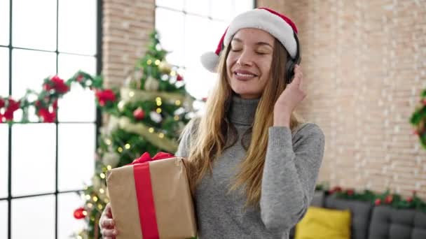 Fiatal kaukázusi nő hallgat zenét tartja karácsonyi ajándék tánc otthon - Felvétel, videó
