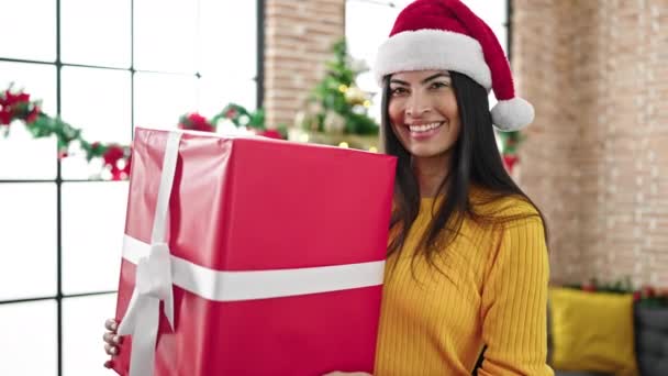 Νεαρή όμορφη ισπανόφωνη γυναίκα γιορτάζει τα Χριστούγεννα κρατώντας δώρο στο σπίτι - Πλάνα, βίντεο