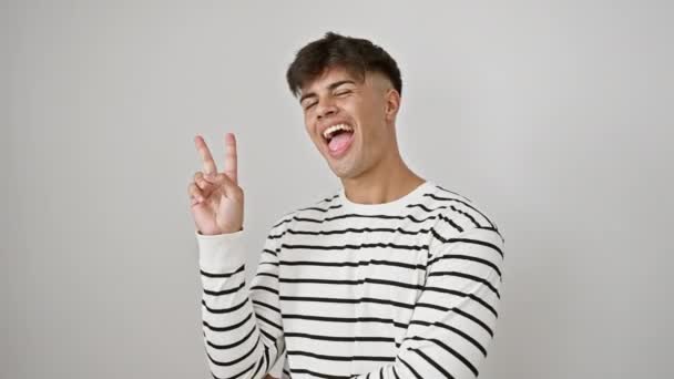 Fröhliche junge hispanische Mann in Streifen, blinkt ein siegreiches Zwei-Finger-" v "-Zeichen und zwinkert, tränkt Zuversicht über einem isolierten weißen Hintergrund. - Filmmaterial, Video