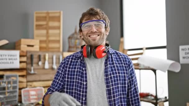 Cheerful young carpenter, expression of joy on his face, confidently making an ok sign with fingers through eye, happily looking at his handiwork in carpentry studio. - Footage, Video