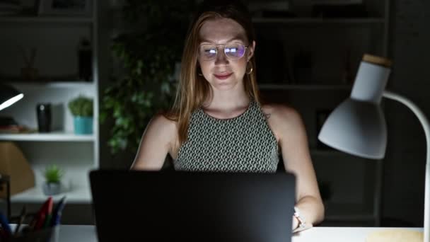 Nuori blondi nainen liiketoiminnan työntekijä, joka käyttää kannettavaa tietokonetta hymyillen toimistossa - Materiaali, video