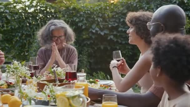 Vrolijke oma hebben plezier chatten met haar grote familie tijdens het diner in de achtertuin op zomeravond - Video