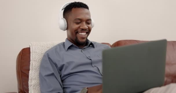 Headphones, laptop and man on sofa for work from home with music streaming, relax and mental health. Happy professional, entrepreneur or african person listening to audio on computer and living room. - Footage, Video