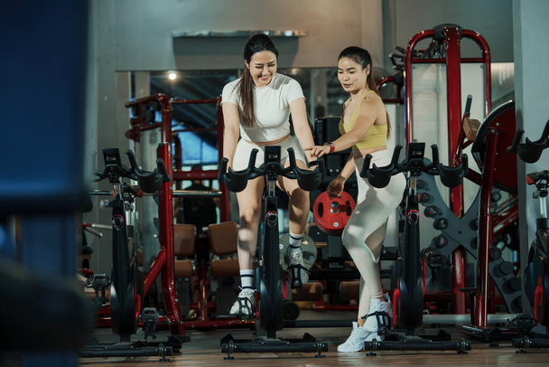 Mujer joven en bicicleta estática con entrenador en el gimnasio. - Foto, Imagen