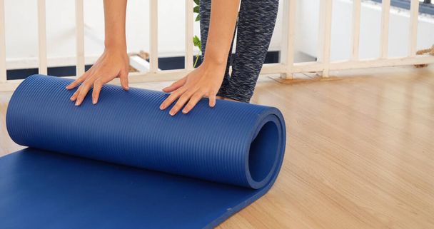 Kadın elleri yoga antrenman odasında jimnastik zemininde yoga minderini sardı. Egzersiz yapan kadın, köpüklü yoga paspası saran elleri kapıyor. Kadın yalınayak evde spor yapıyor sağlıklı yaşam tarzı konsepti - Fotoğraf, Görsel