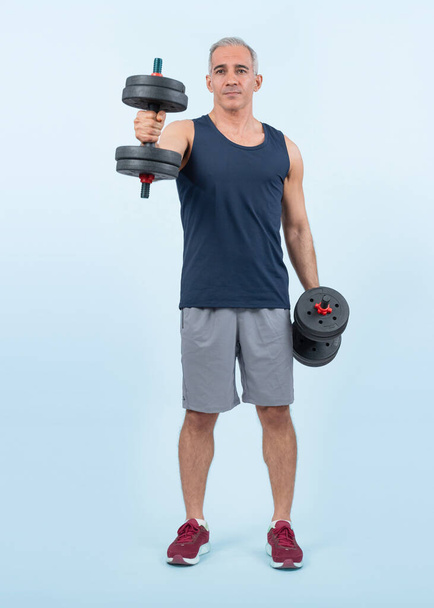 Full body length shot active and sporty senior man lifting dumbbell during weight training workout on isolated background. Healthy active physique and body care lifestyle for pensioner. Clout - Photo, Image