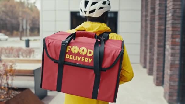 Вид из-за среднего отслеживания снимок парня доставки еды, идущего по улице в городской зоне, оглядывающегося вокруг - Кадры, видео