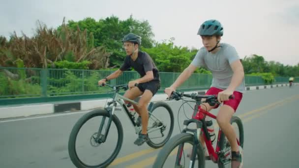 Мальчик-подросток в защитном шлеме и спортивной одежде катаются на велосипеде вместе с папой на открытом воздухе в летний день - Кадры, видео