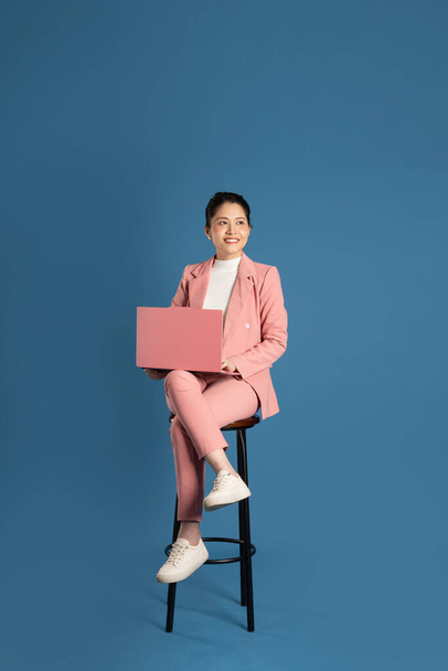 Προσωπογραφία της νεαρής επιχειρηματία που κάθεται στην καρέκλα και απομονώνεται σε μπλε φόντο - Φωτογραφία, εικόνα