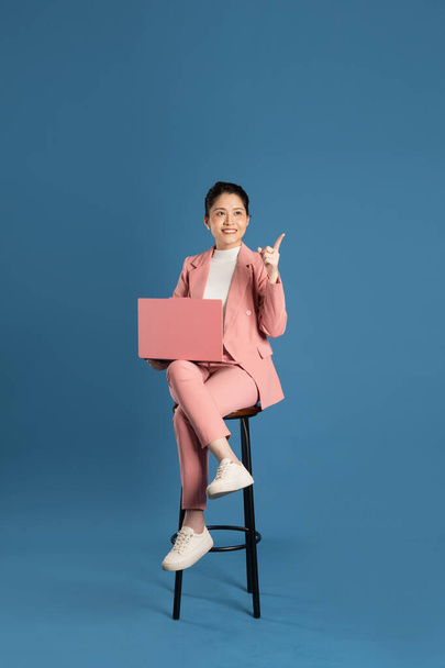 Portrait of young businesswoman sitting in chair and isolated on blue background - Foto, Bild
