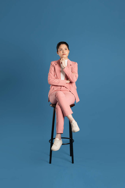 Portrait of young businesswoman sitting in chair and isolated on blue background - 写真・画像