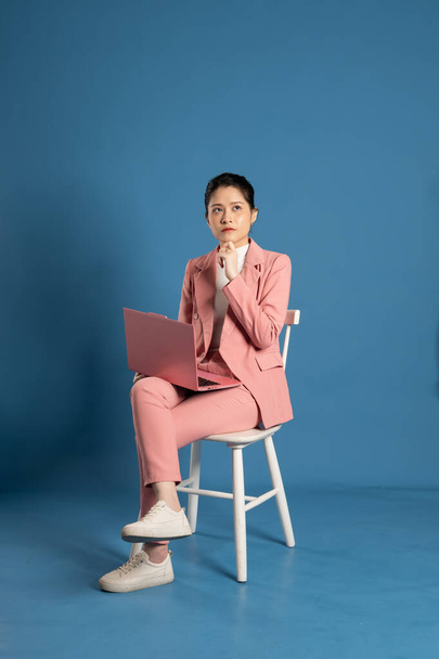 Портрет молодой предпринимательницы, сидящей в кресле и изолированной на синем фоне - Фото, изображение