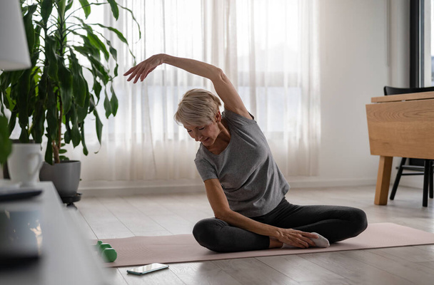 Actieve senior vrouw die yoga binnen beoefent - Foto, afbeelding