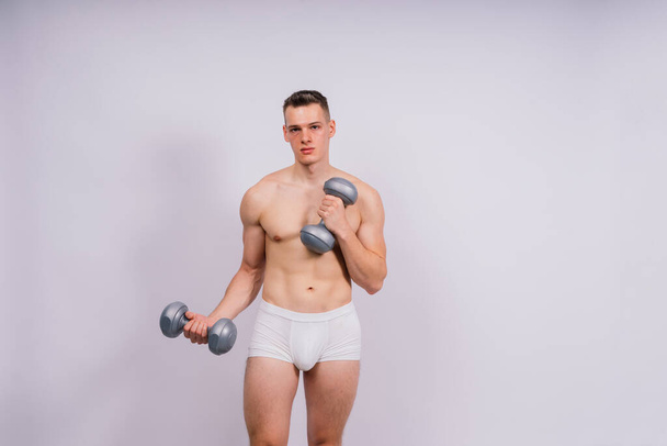 Студийный снимок мускулистого молодого человека, тренирующегося с гантелями на сером и черном фоне. - Фото, изображение