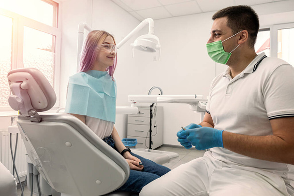 здоровий жіночий пацієнт, який щасливо посміхається в стоматологічному кабінеті поруч із стоматологом. зуби стоматології
 - Фото, зображення