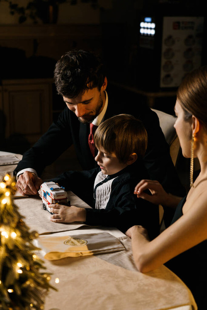 Hyvää joulua! Onnellinen perhe syö päivällistä kotona. Juhlaloma ja yhdessä oleminen puun lähellä.Isä, äiti ja poika joulupöydässä. Joulun ja uudenvuoden käsite - Valokuva, kuva