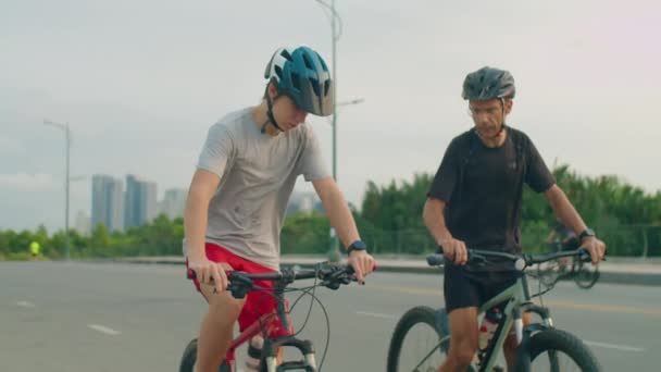 Отец и сын-подросток катаются на велосипеде по дороге, отдыхают и пьют воду во время езды на велосипеде в летний день - Кадры, видео
