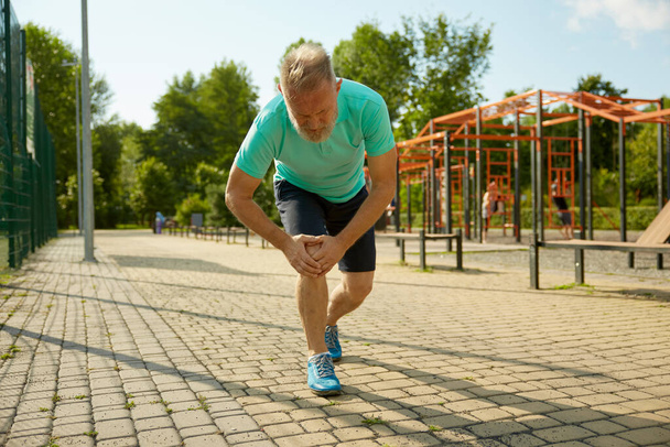 Senior sportsman suffering with knee having injury during jogging workout. Sprain ligament or meniscus elderly health problem - Photo, Image