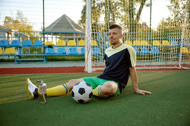 Young sportive man relaxing after soccer game training. Goalkeeper waiting for team and start second half of football match - Photo, Image