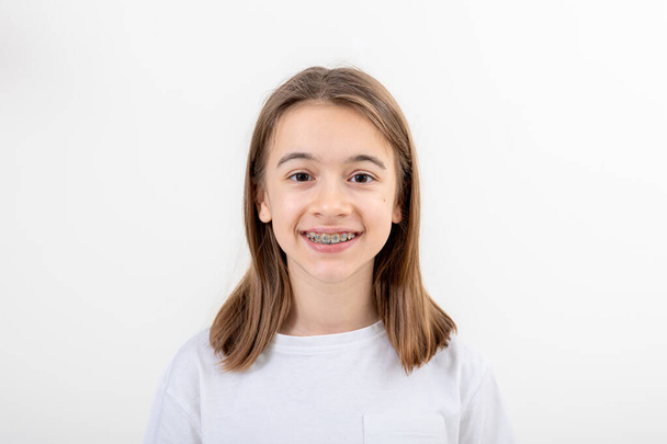 Brunette Kaukasisch meisje glimlachen met beugels op haar tanden op een witte achtergrond geïsoleerde, tandheelkundige gezondheid concept. - Foto, afbeelding