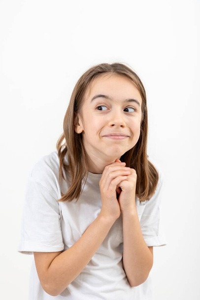 A funny teenage girl in a white T-shirt looks interestedly to the side on a white background isolated. - Foto, Imagem
