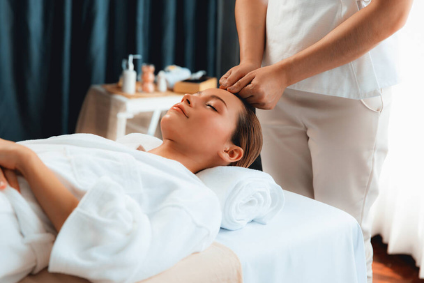 Caucasian woman enjoying relaxing anti-stress head massage and pampering facial beauty skin recreation leisure in dayspa modern light ambient at luxury resort or hotel spa salon. Quiescent - Photo, Image