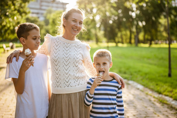 Güneşli bir günde parktaki iki oğluyla mutlu bekar anne portresi. Çocuklar dondurma yiyor.. - Fotoğraf, Görsel