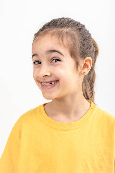 Маленька кавказька дівчинка в жовтій футболці посміхається і дивиться на камеру на білому тлі ізольовано. - Фото, зображення