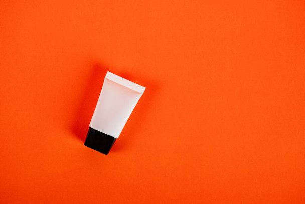 Plastic white tube for cream or lotion. Skin care or sunscreen cosmetic on orange background. - Photo, Image
