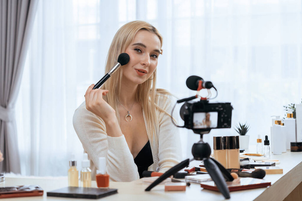 Young woman making beauty and cosmetic tutorial video content for social media. Beauty blogger smiles to camera while showing how to apply mascara to audience or followers. Blithe - Photo, Image
