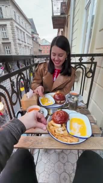 felice coppia mangiare hamburger in caffè al balcone al di fuori carino città europea - Filmati, video