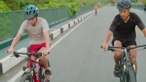 Father and son in protective helmets and sportswear cycling along road during bike ride outdoors on summer day - Footage, Video