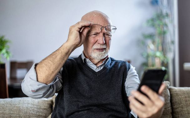 Az idősebb férfi zavartan bámulja az okostelefonját. - Fotó, kép
