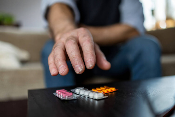 Primo piano dell'uomo che prende pillole sul divano a casa in soggiorno - Foto, immagini