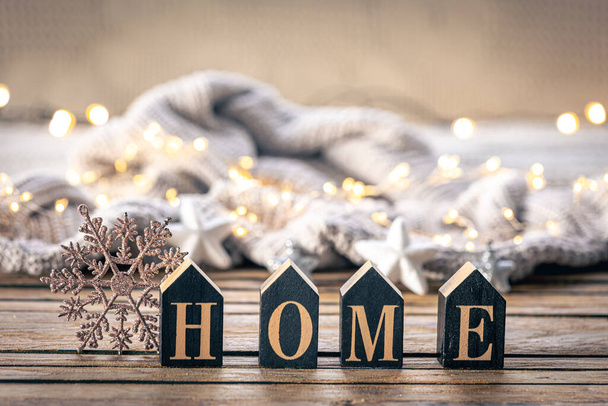 Przytulne zimowe tło z dekoracyjnym słowem Home wykonane z drewnianych liter na rozmytym tle z girlandą z dzianin elementów. - Zdjęcie, obraz
