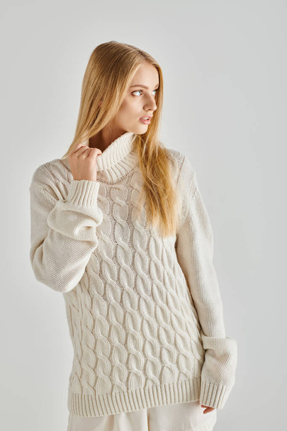 young dreamy woman with blonde hair posing in soft knitted sweater and looking away on grey, winter - Photo, Image