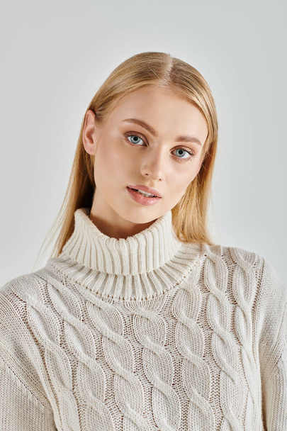 portrait of beautiful blonde woman in  white knitted sweater looking at camera on grey, winter style - Photo, Image